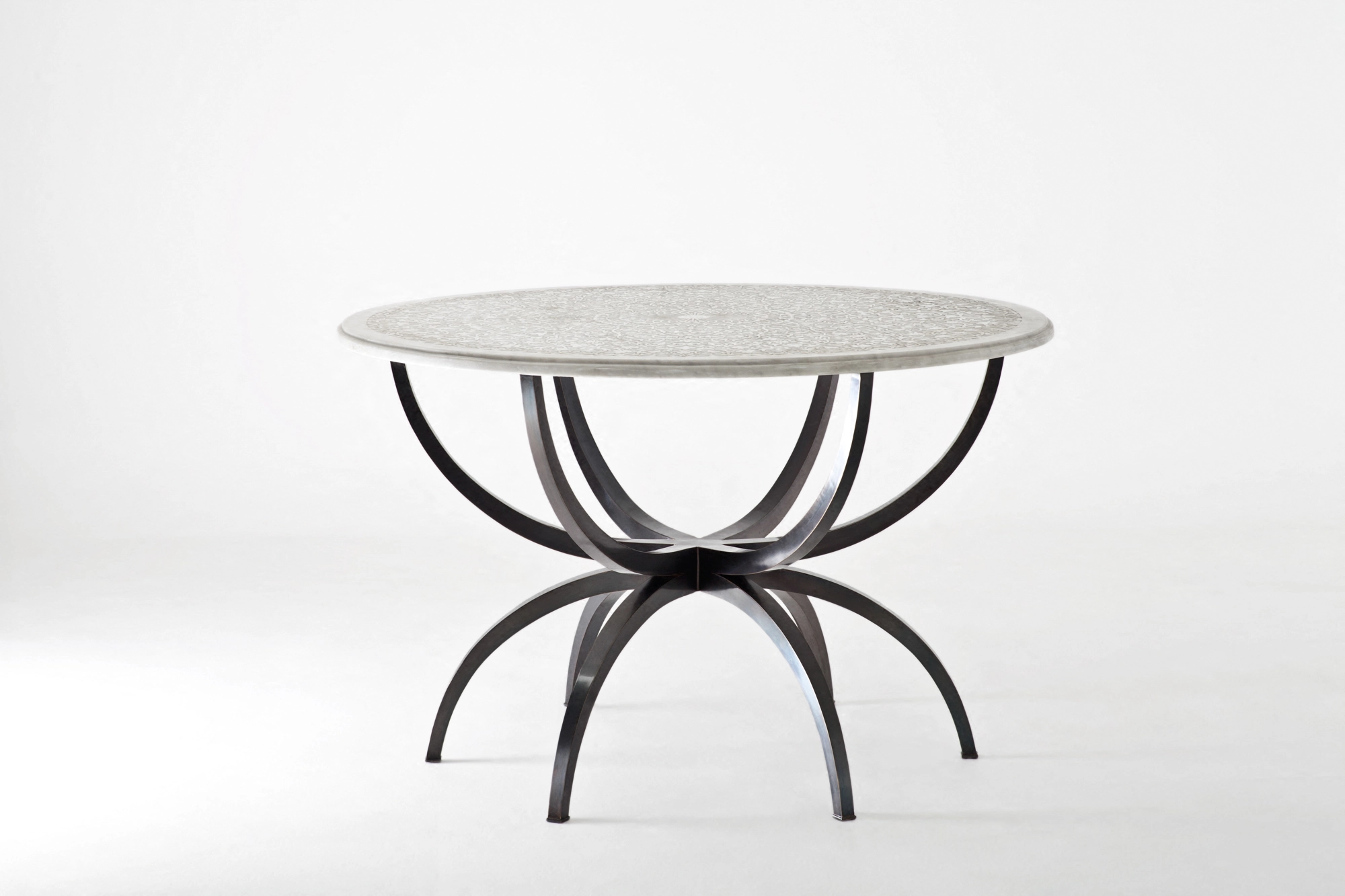 A round table with a pale engraved top on curved dark iron legs, against a white background.
