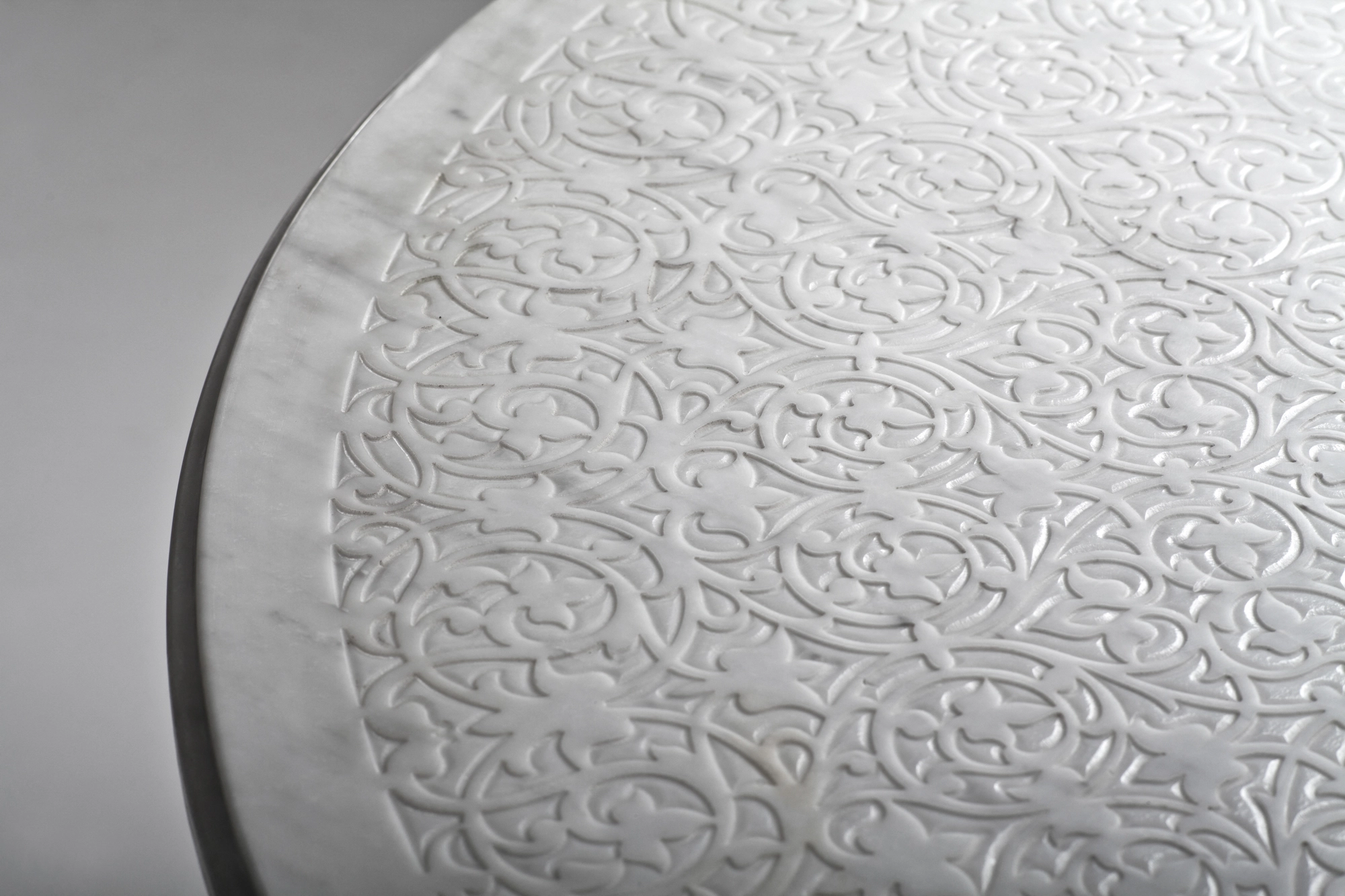 Close-up of a round pale tabletop's finely engraved surface and bevelled edge.