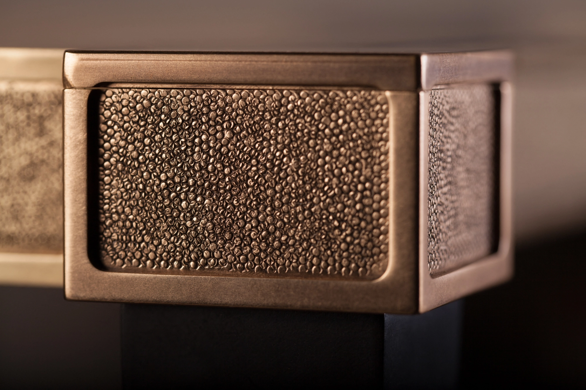 Close-up of a console table's bronze leg-top inset with a textured shagreen panel.