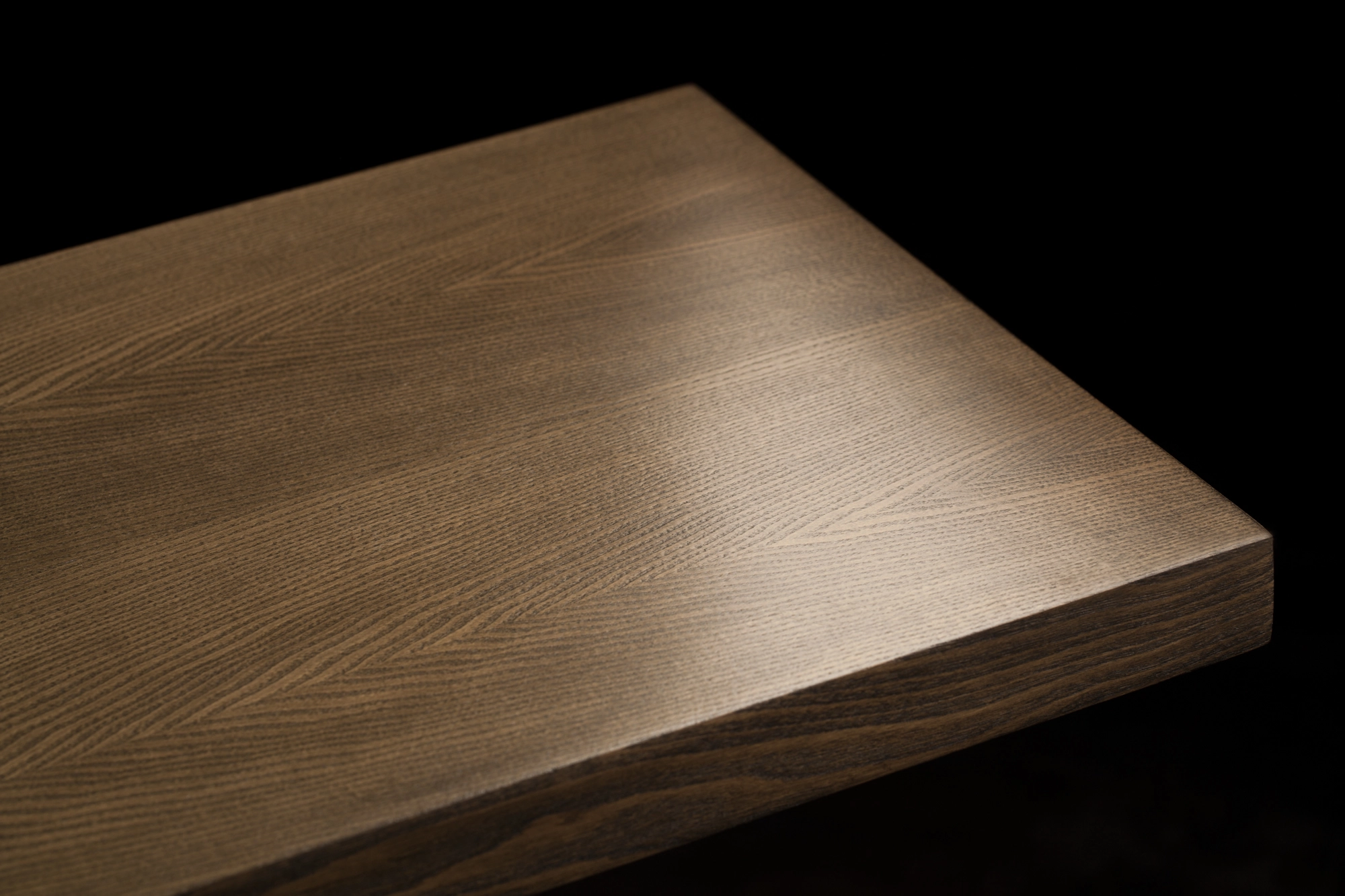 Close-up of a wooden console table's grained top corner, lit against a dark background.