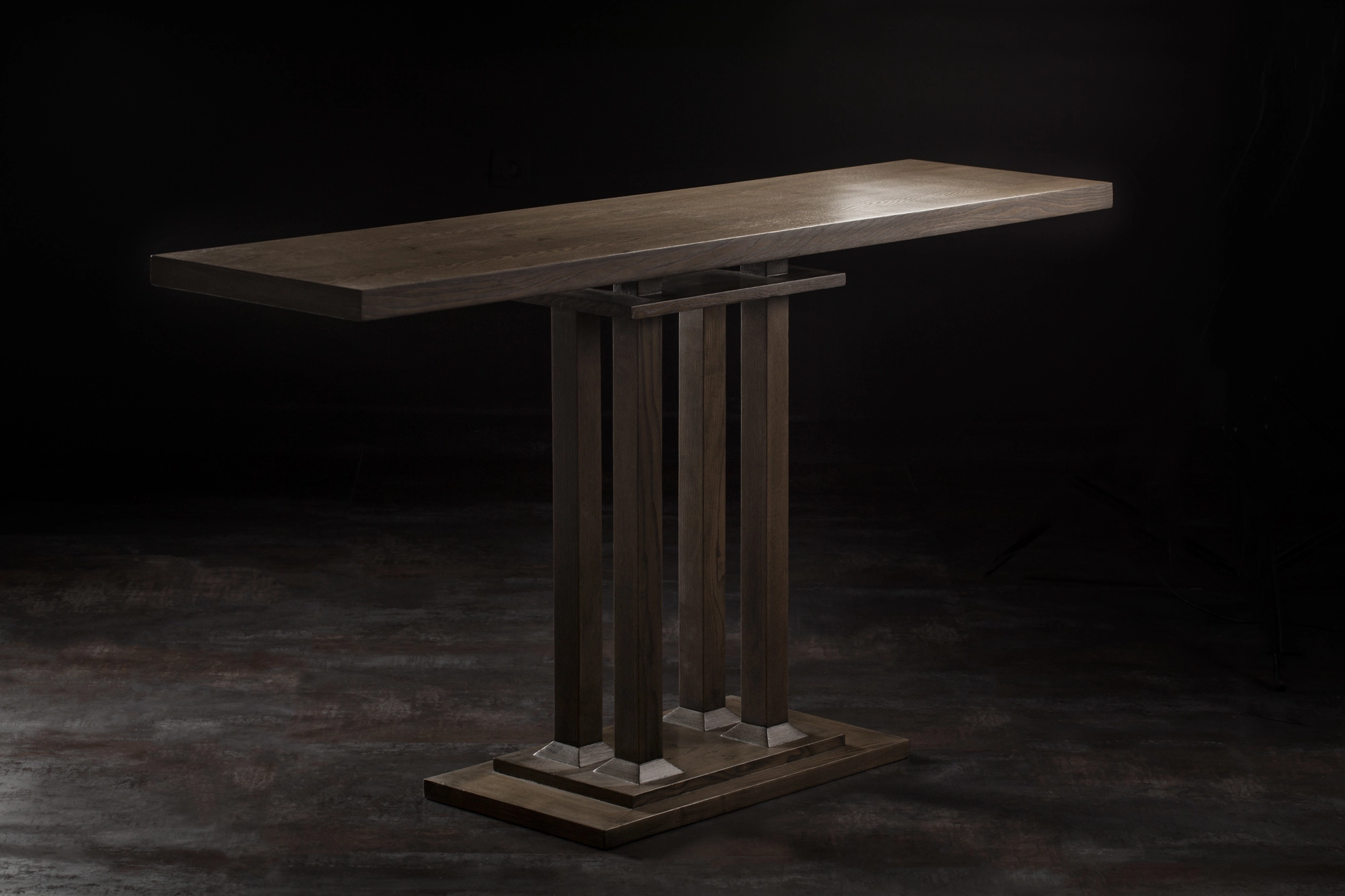A wooden console table with a slatted multi-column pedestal base, lit against a dark background.