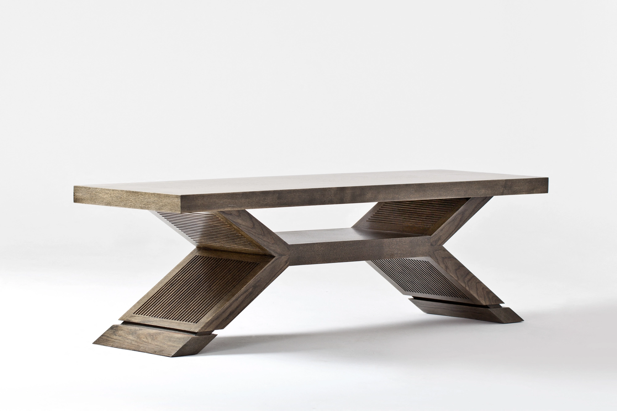 A low wooden coffee table on an angular cross-shaped base, seen from the side against white.