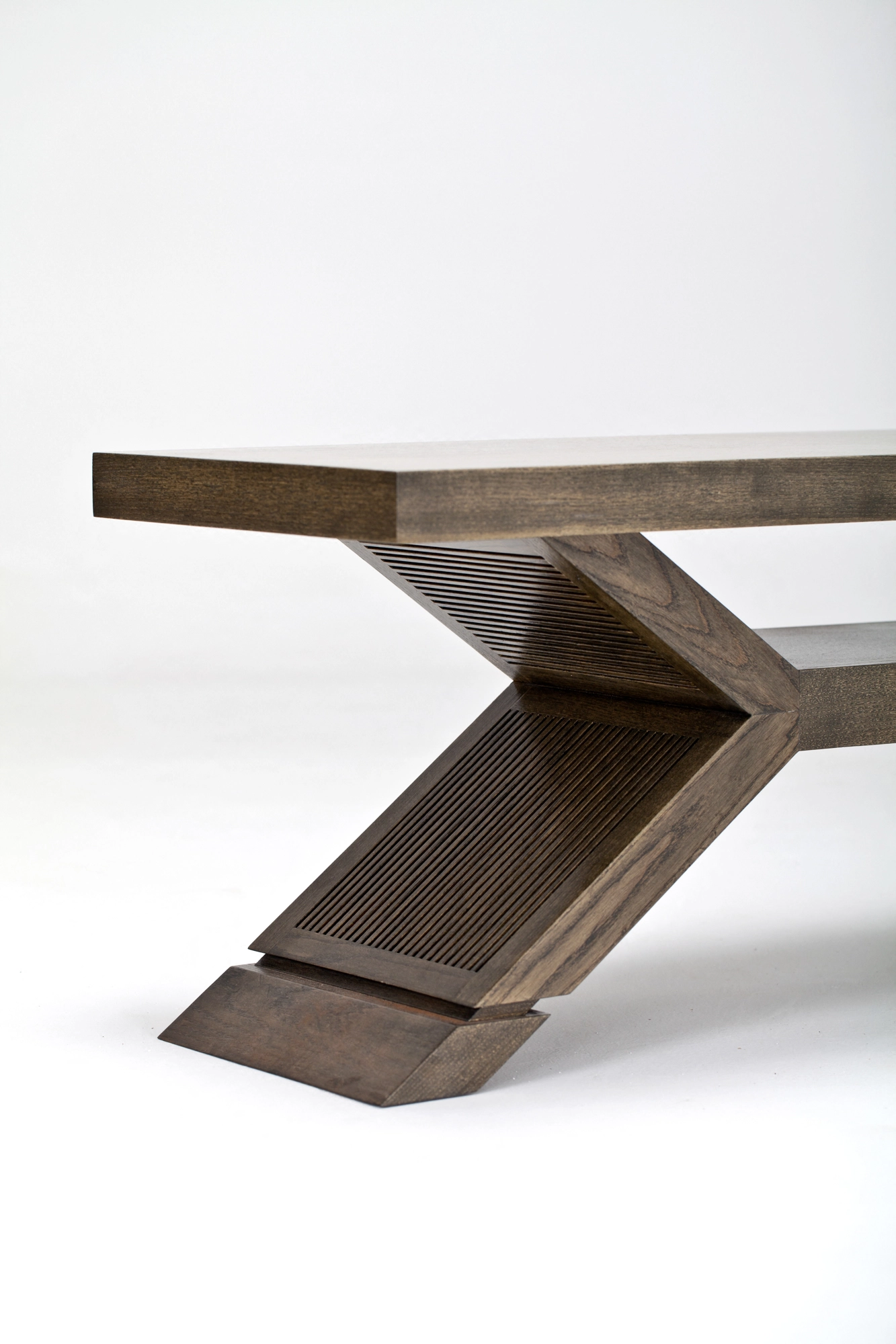 Close-up of a wooden coffee table's angular Z-shaped pedestal base and stacked timber layers.
