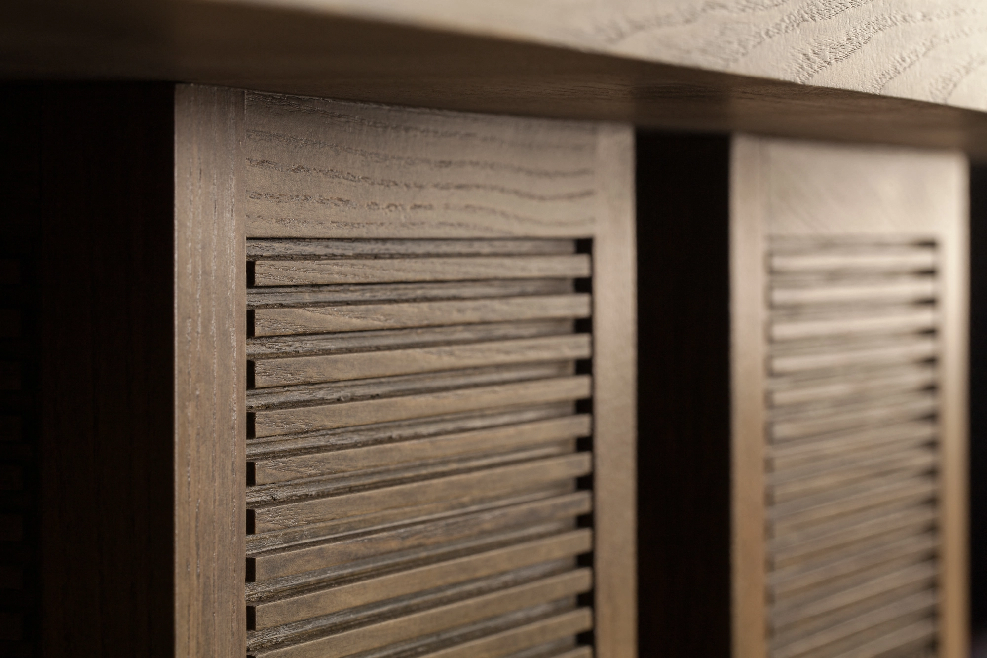 Close-up of finely slatted wooden panels on a cabinet, lit to show the vertical ribbing.