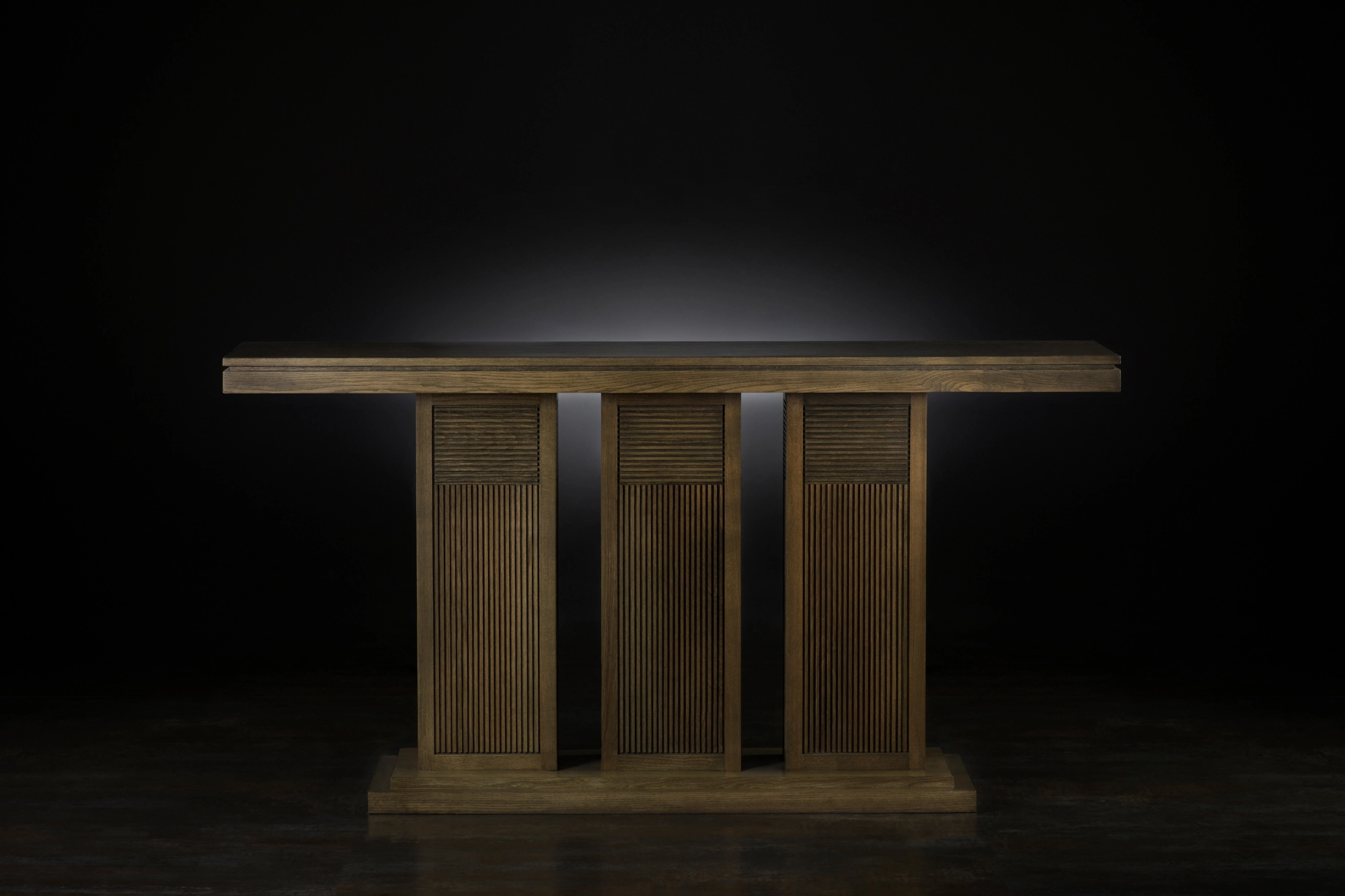 A wooden console table on a slatted three-column base, lit against a dark background.