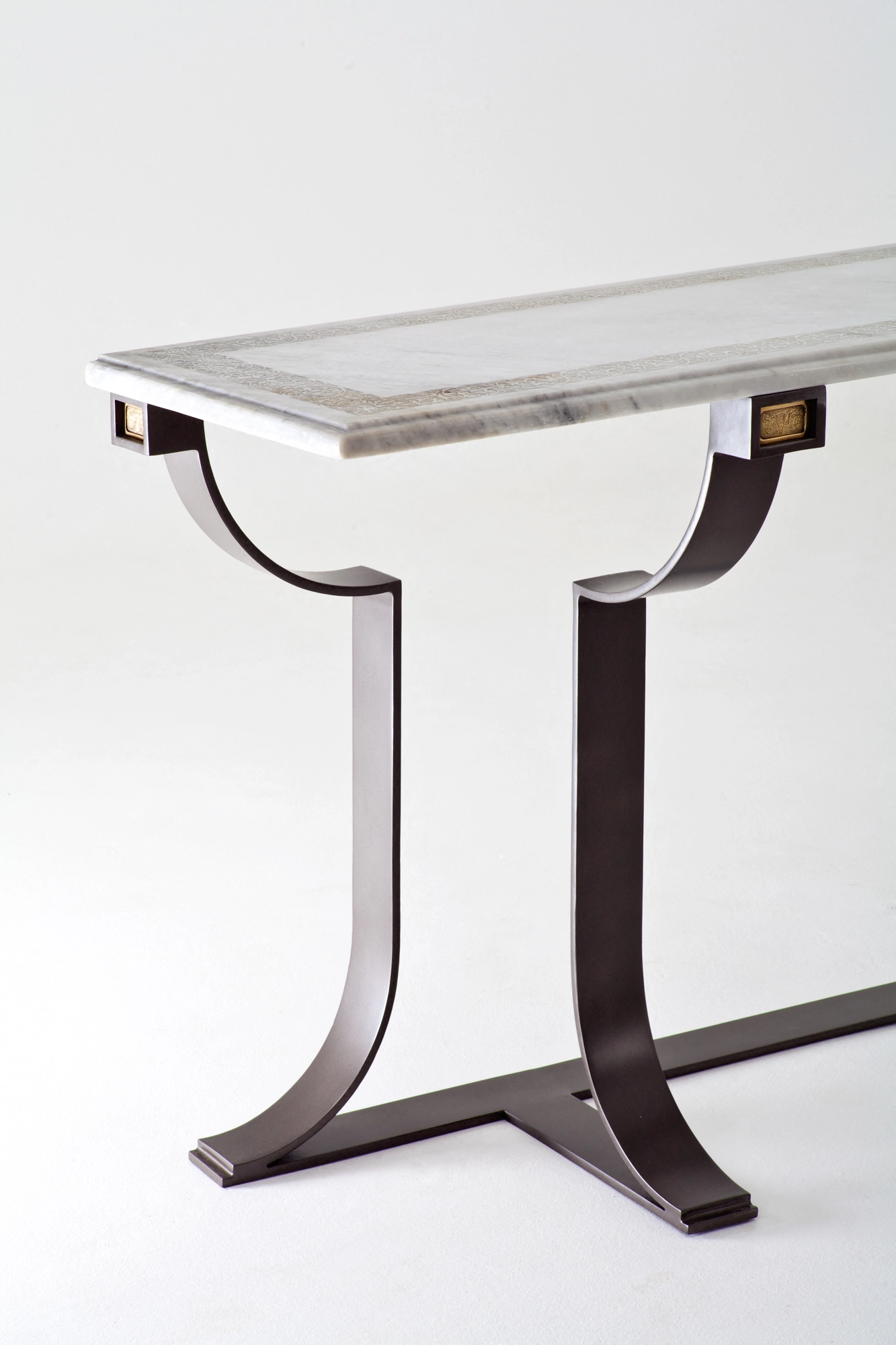 A console table's curved dark metal leg supporting a pale carved stone top, against a white background.