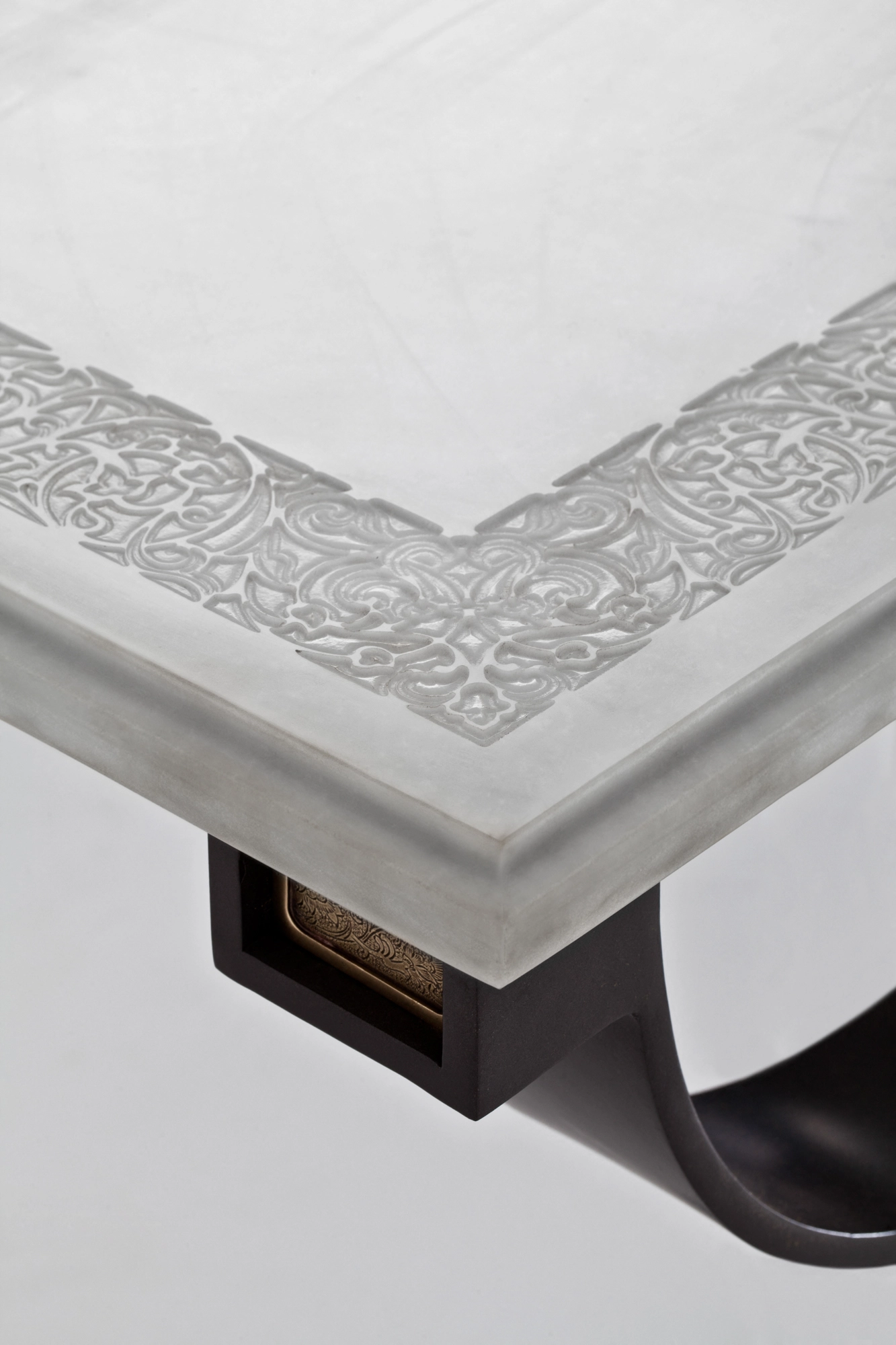 Corner detail of a console table where the pale carved stone top meets a dark curved metal leg.