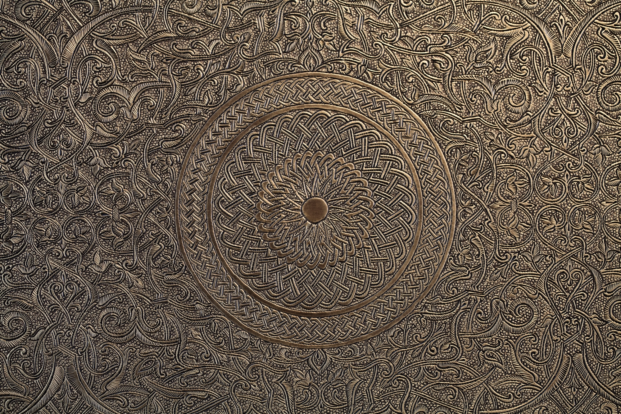 Close-up of an engraved bronze panel worked with a dense circular medallion pattern.