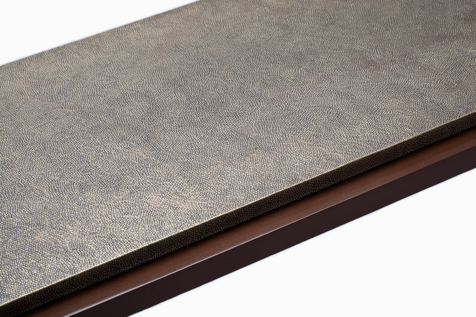 Edge detail of a console table's textured grey top finished with a thin brass trim.