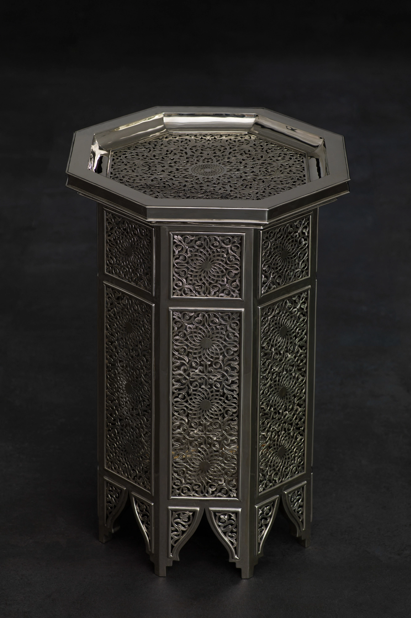 An octagonal engraved silver occasional table seen from above at an angle, against a black background.
