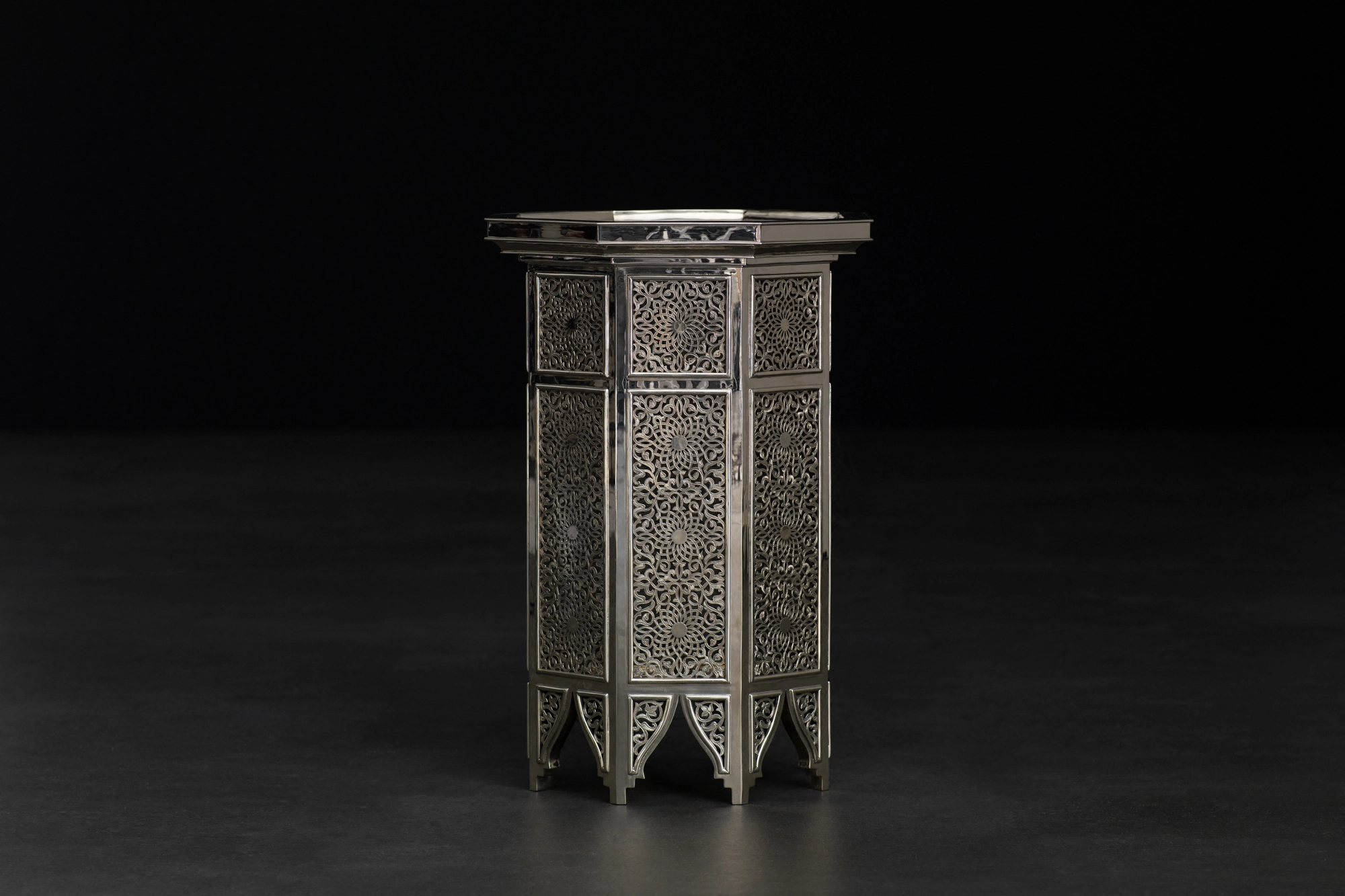 An octagonal engraved occasional table with a tray top and arched feet, against a black background.
