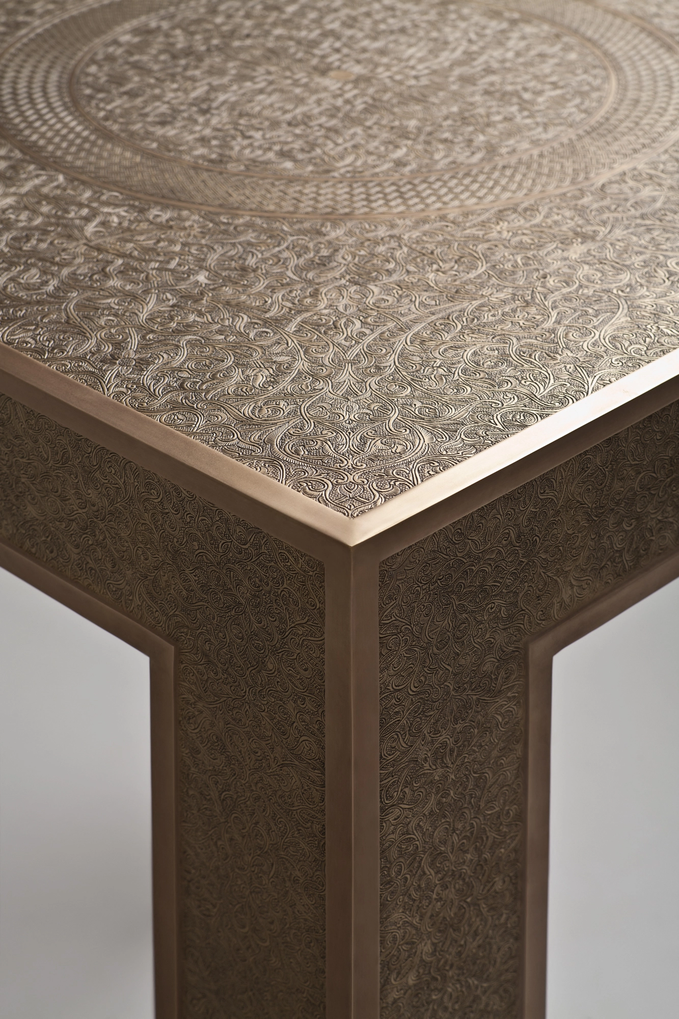 Close-up of an engraved-metal occasional table's top corner meeting its tapered leg.