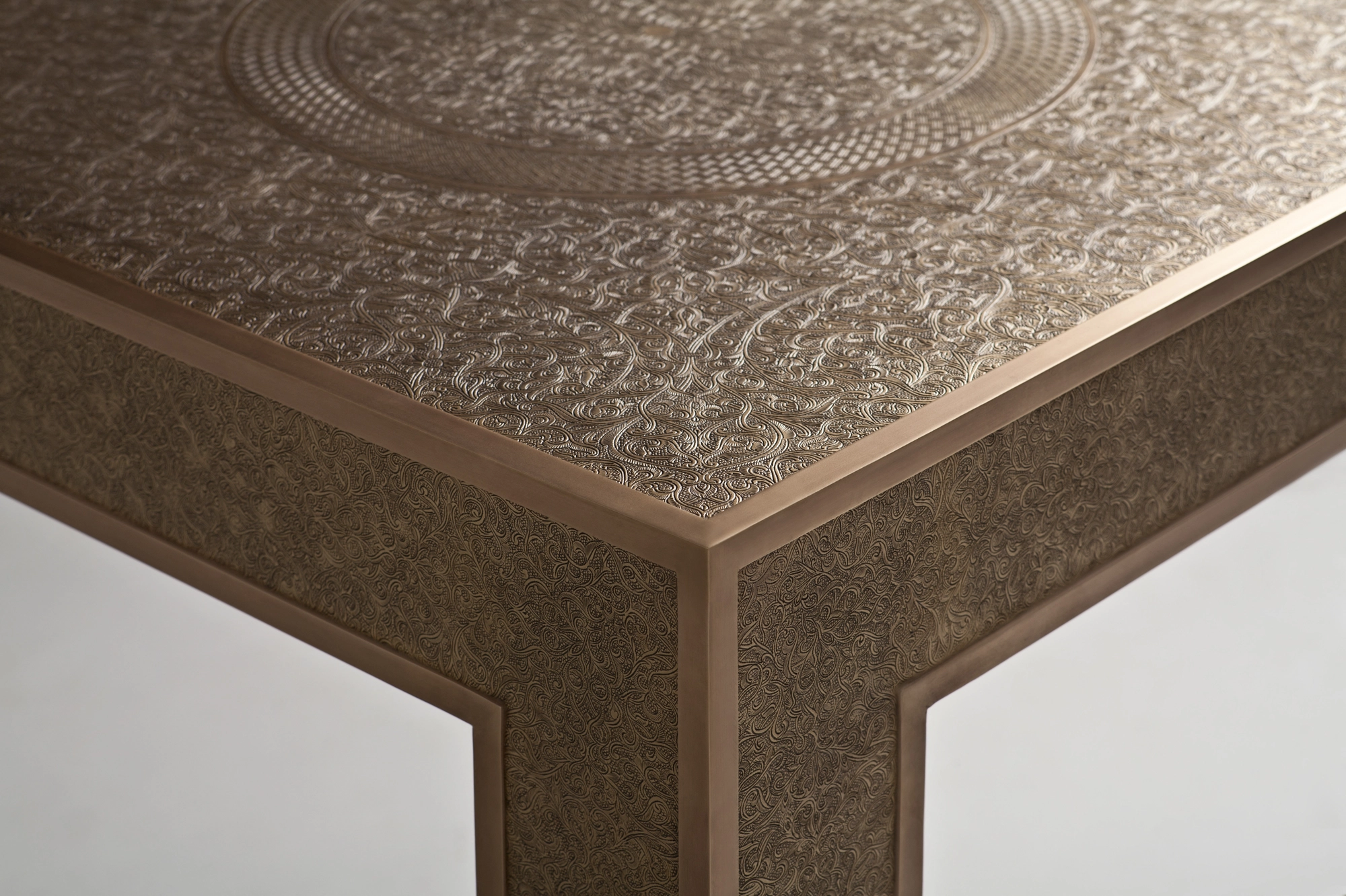 Close-up corner of a pale engraved-metal occasional table showing its patterned top and edge.