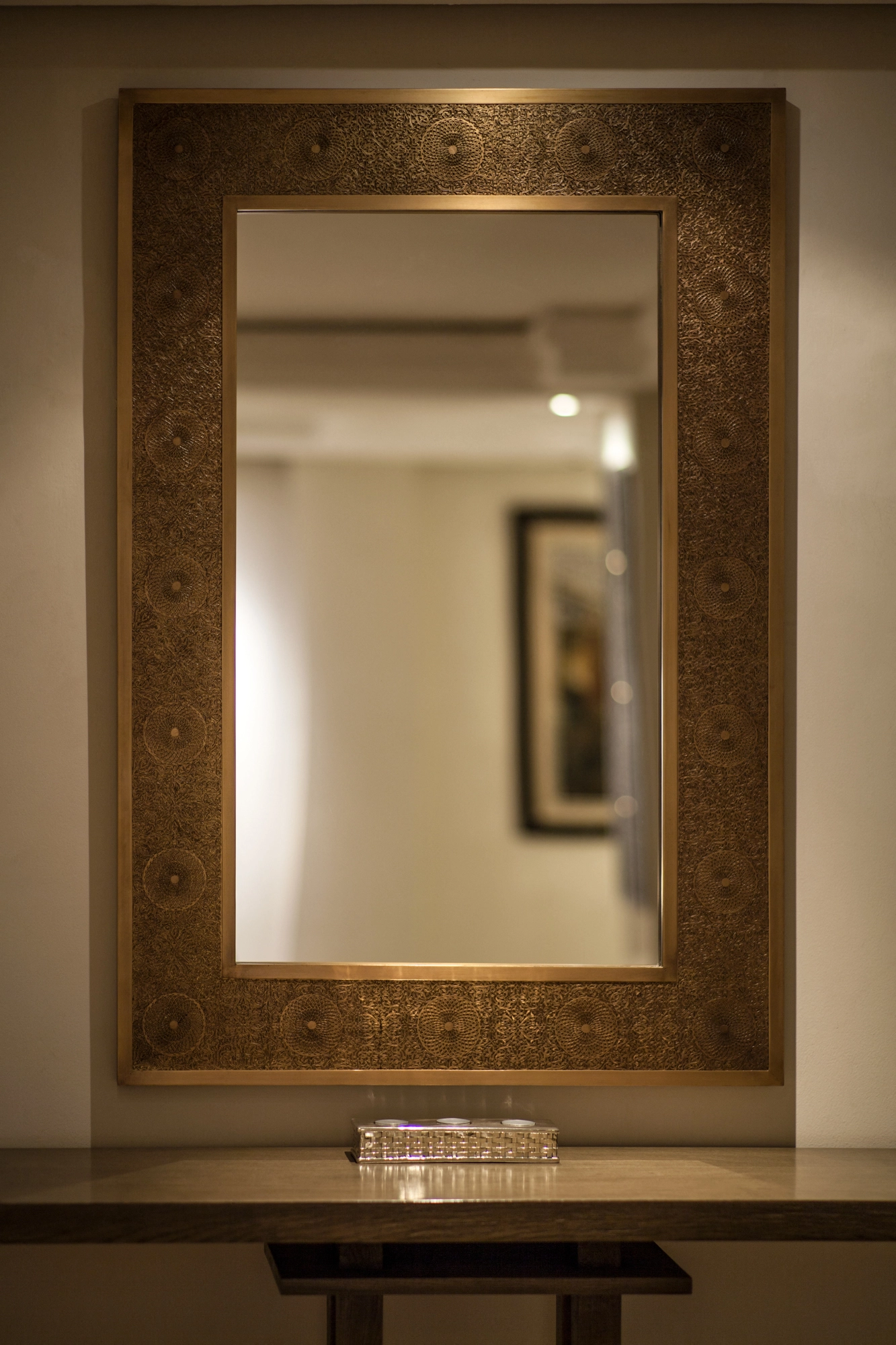 A tall rectangular mirror in an ornate gilded openwork frame above a console table in a warmly lit room.