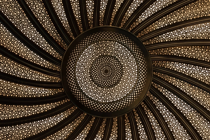 Radiating sunburst disc of perforated gold metal with a fine dotted spiral pattern, Cosmic Spiral 818 series.