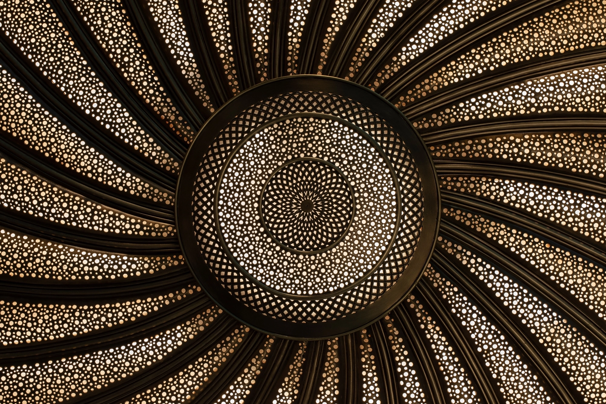 Radiating sunburst disc of perforated gold metal with a fine dotted spiral pattern, Cosmic Spiral 818 series.