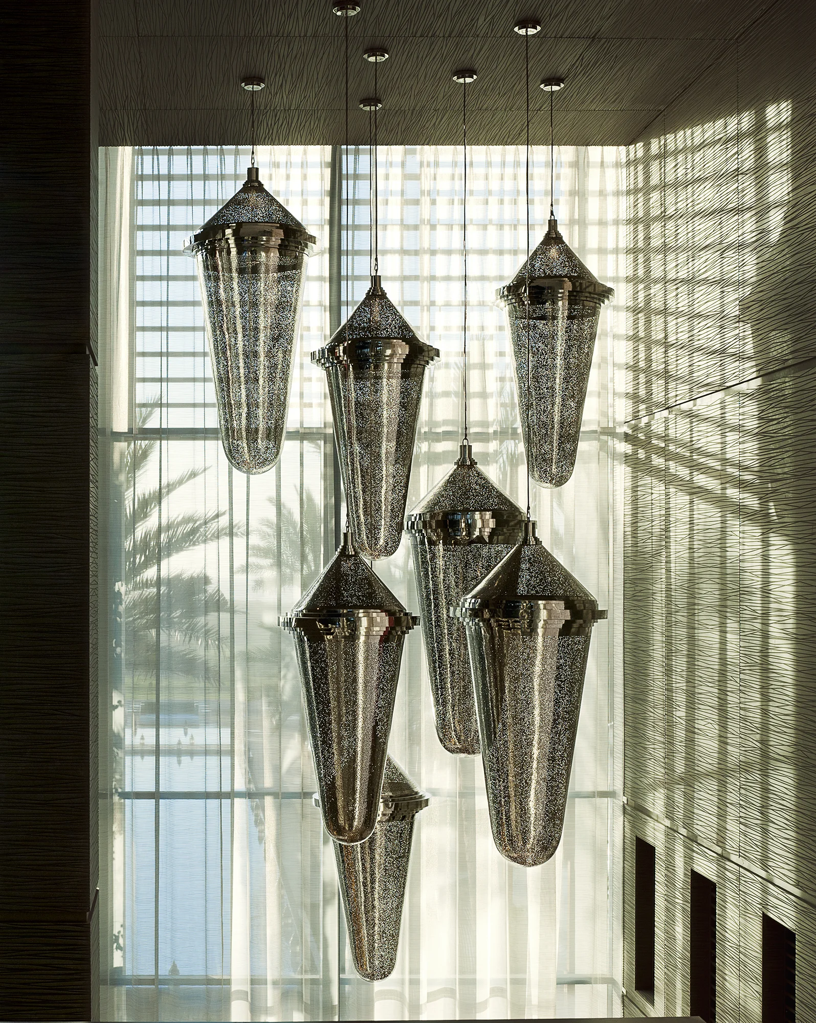 A cluster of pierced metal amphora-shaped pendant lights cascading in front of a tall latticed window.