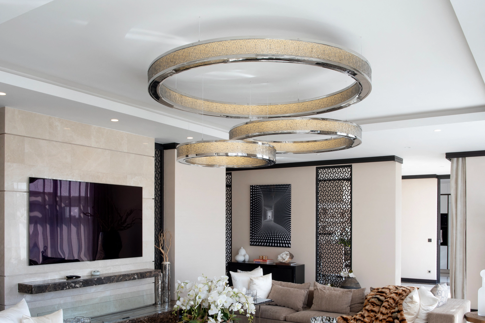 Modern living room with two circular ring chandeliers above a neutral sofa and wall-mounted screen.
