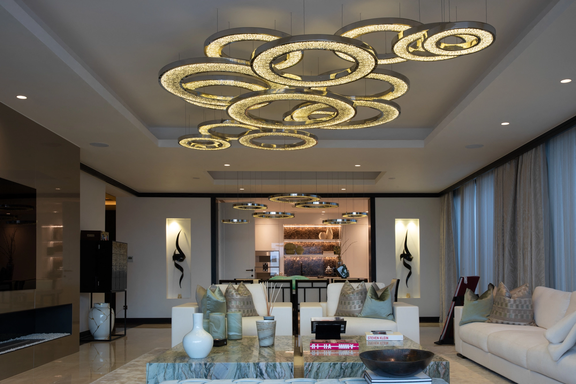 Living room crowned by a cluster of gold ring chandeliers above pale sofas.