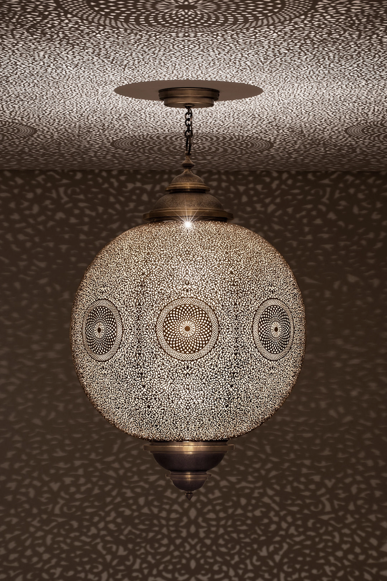 A spherical pierced metal pendant lamp lit from within, scattering dappled dotted light across the ceiling.