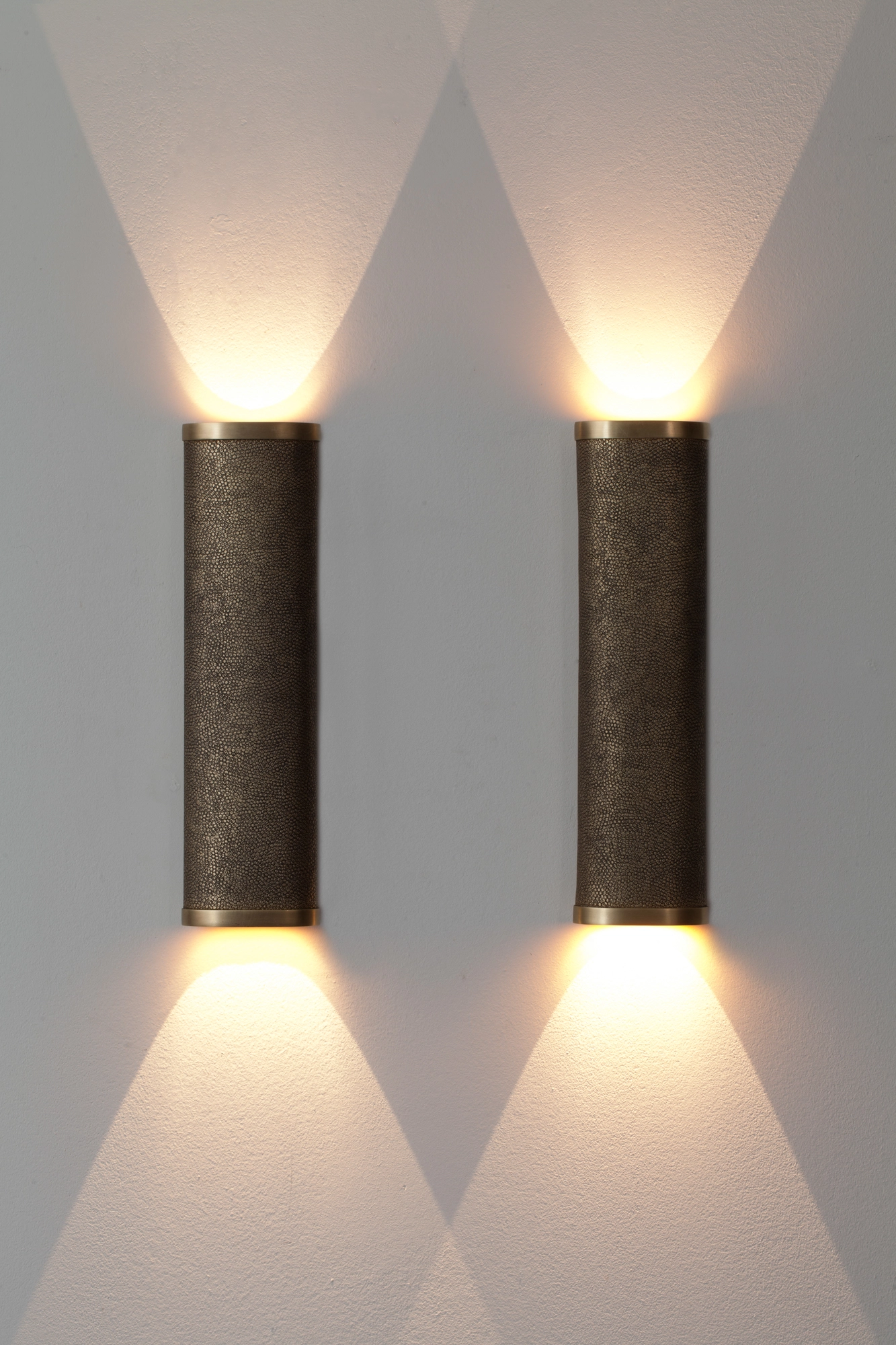 Pair of textured cylinder wall lights casting crisp triangular cones of light up and down a grey wall.