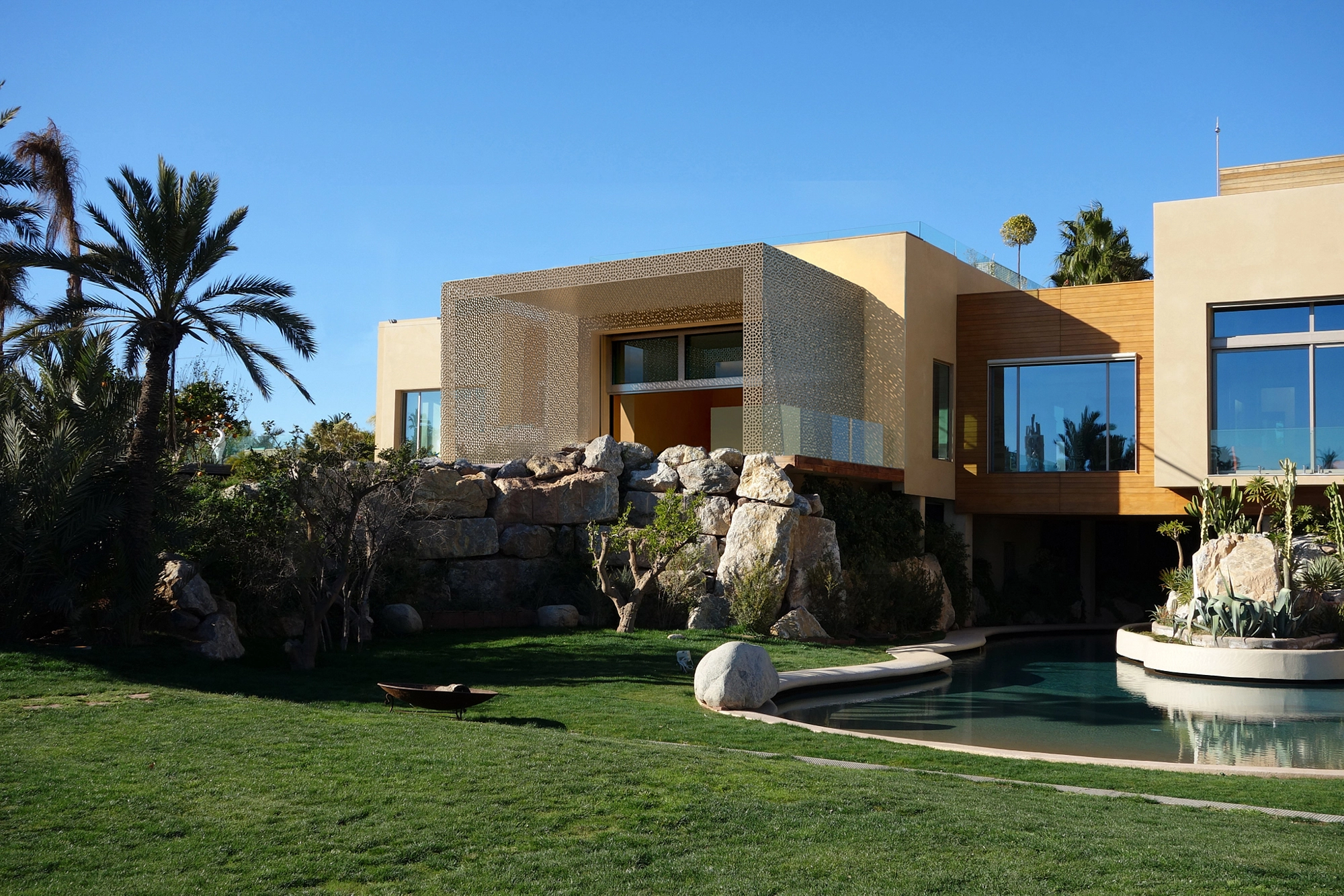 Modern villa beside a rock and water garden with a green lawn under a clear blue sky.