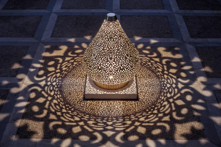 Teardrop-shaped pierced-metal Floral Lotus sculpture on a dark tiled floor, casting floral shadow patterns.