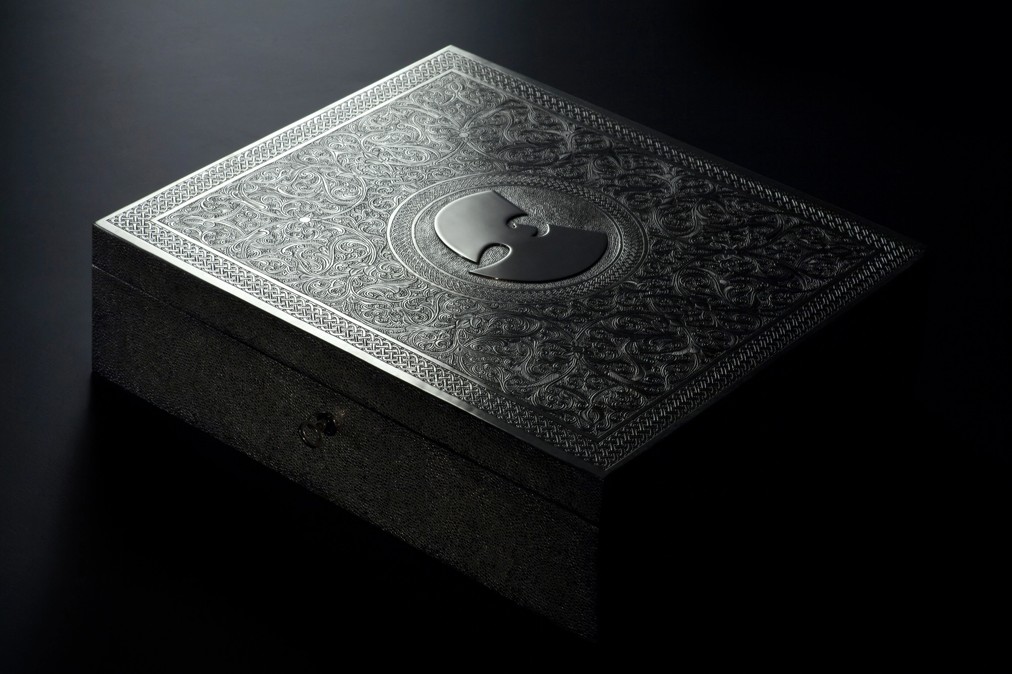 A closed engraved silver box with a stylised emblem on its lid, lit against black.